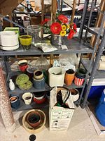 Overview of shelving with assorted planters, metal bucket with artificial flowers, boxed sprayer at bottom