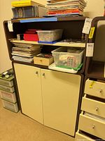 Stacked brown frame cream front modular shelving cabinet and open shelf pieces with assorted contents shown for scale