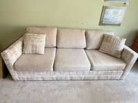 Full front view of beige three-cushion sleeper sofa with two throw pillows