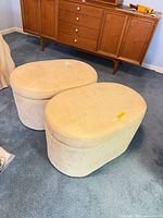 Two matching cream oval storage ottomans closed, near mid-century dresser
