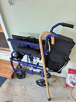 Folded blue Medline transport chair with wooden cane leaning against it