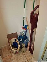 Group of cleaning tools in closet including stick vacuum, bug vacuum, mop handles, buckets