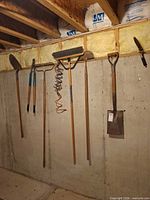 Overall view of six hanging long-handle tools on basement wall