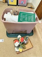 Overall view of bin, lid beneath, crocheted vegetables and metal pitcher beside