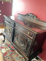 Front and side angle of carved sideboard showing drawers, doors, crest, legs