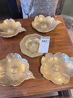 Group of four flower-form brass bowls and one hexagonal brass dish on wooden surface