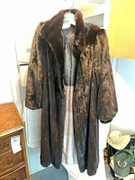Full view of dark brown fur coat hanging, showing length, sleeves, lining, and label