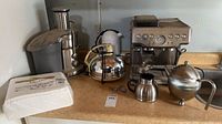 Countertop view showing juicer, electric kettle, stovetop kettle, teapot, creamer, thermos, tea infuser, napkins and espresso machine