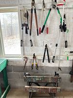 Wall-mounted view of multiple loppers, hedge shears and folding workbench below