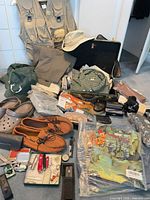 Assorted clothing, shoes, hats, Swiss Army knives, hard case displayed on floor