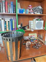 Wide view of shelving with lamp, waste basket, bookends, speakers, supplies