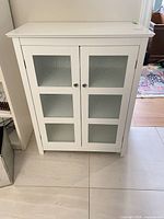 Front view of white cabinet showing two glass panel doors and knobs