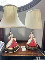Pair of bedside lamps featuring porcelain lady figurine bases, brass-tone bases, and cream shades