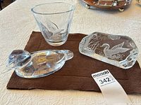 Lot overview showing three glass items: duck figurine, etched tumbler, etched paperweight