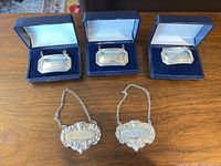 Five sterling silver decanter tags, three rectangular in boxes, two ornate, all with chains