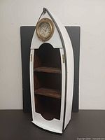 Front view of boat-shaped shelf displaying clock and two shelves