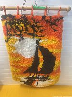 Front view of latch-hook sailboat sunset wall hanging on wood dowel