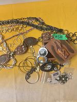 Overview of belts, necklaces, earrings, brooch, wood box and packaged jewelry on yellow surface