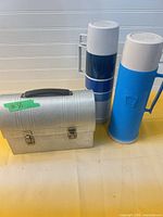 Front view of aluminum lunch box and two plastic Thermos bottles