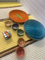 Group shot of orange and blue wicker trays, six small bowls, Rubik’s Cube