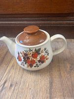 Side view of ceramic teapot showing fruit floral design and lid
