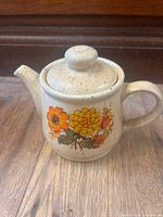 Front view of speckled stoneware teapot with floral design and lid on