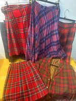 Group of five kilts and tartan blazer displayed on hangers