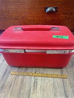 Closed red Samsonite train case front view beside ruler