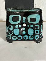 Front view of black ceramic ikebana vase with turquoise geometric pattern, central hole visible