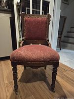 Front view of chair showing red upholstery, carved wood, turned legs