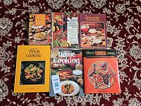 Front covers of all six cookbooks arranged on patterned carpet
