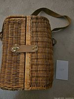 Side view of wicker wine carrier showing leather turn-lock clasp and woven body