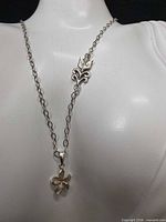 Necklace displayed on bust showing chain, fleur-de-lis accent, flower pendant
