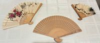 Full view of three folding fans laid out: carved wood, rose-painted, bamboo-painted