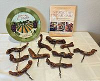 Group shot showing ten corkscrews, decorative plate, and book