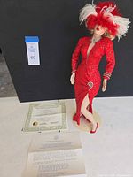 Full view of doll on stand with certificate and paperwork