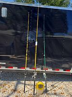 Three fishing rods standing upright against trailer with bait bucket at base