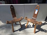 Front view of both rustic solid wood birthing chairs showing seat, legs, tall backrests with clover cut-outs