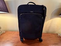 Front view of black Tumi rolling carry-on with front zip pocket and wheels visible