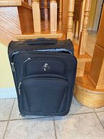 Front view of black Atlantic carry-on suitcase showing front zip pocket and logo