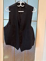 Front of black formal vest showing five buttons, welt pockets, pointed hem