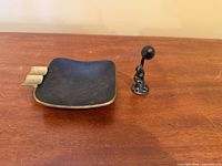 Top view of black enamel brass ashtray with pipe tamper upright beside it