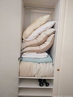 Stacked pillows, comforter and quilt inside closet