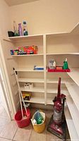 Pantry shelves with vacuum, bucket, mop, cleaning bottles, kitchen wraps