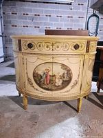 Overall front view of demilune cabinet showing shape, painted decoration, legs