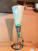 Full view of lamp on tabletop showing metal tripod base, conical body and shade