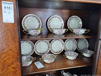 Cabinet shelf showing seven double-handled bowls and eight saucers in matching floral pattern
