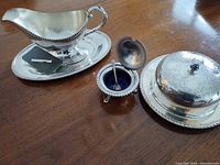 Gravy boat on oval underplate, butter dish, condiment pot with opened lid and spoon