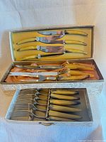 Open case showing top tray of six steak knives, middle tray of large utensils and lower tray of forks
