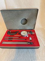 Open case showing dial indicator, clamp, rods, bar and adapter in red foam